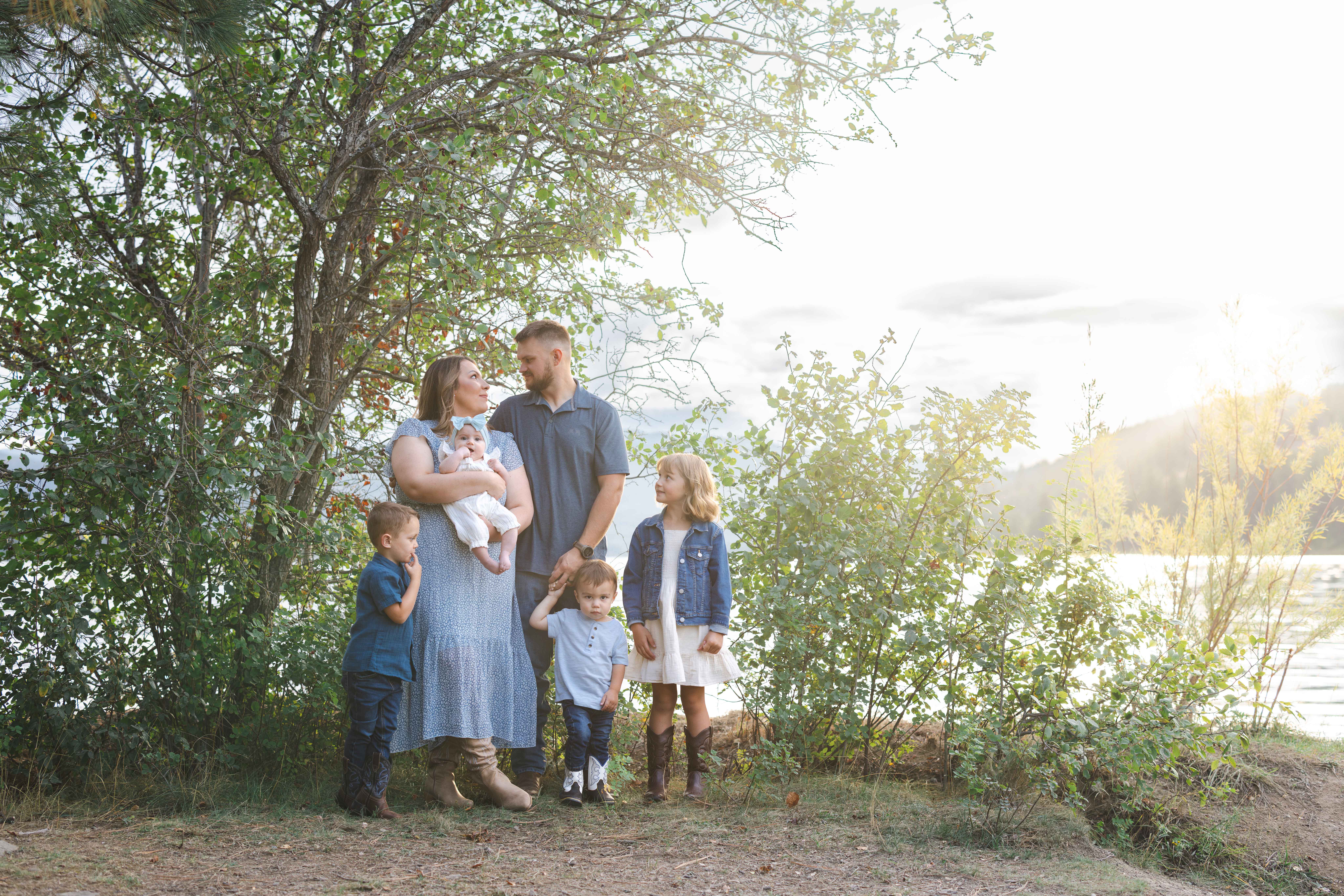 Family standing together under trees along the Pend Oreille River in North Idaho during a warm golden hour photography session